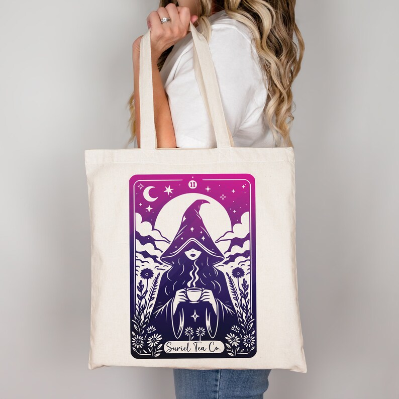 Tarot card design graphic with a mysterious woman wearing a hooded cloak and drinking tea, surrounded by wildflowers, stars and large moon in the sky. Text Suriel Tea Co at the bottom. ACOTAR inspired PNG SVG DXT cut file. Perfect for print on demand
