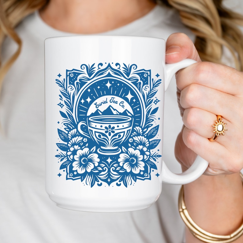 A decorative tarot card design featuring a teacup against a backdrop of mountains and stars, adorned with floral elements. The text reads Suriel Tea Co. ACOTAR inspired graphic. PNG, JPG, DXF Cut File, and SVG. Works in Canva. Gift for fantasy reader
