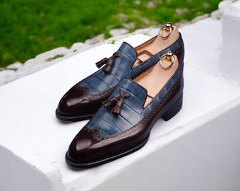 May include: A pair of brown and blue leather tassel loafers with a brogue design. The shoes have a pointed toe and a low heel.