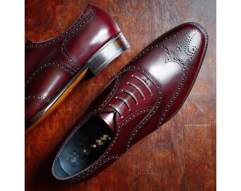 May include: A pair of burgundy leather oxford shoes with brogue detailing and lace-up closures.