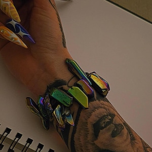 May include: A person's arm with a tattoo of a panda bear wearing a bracelet made of iridescent crystal shards.