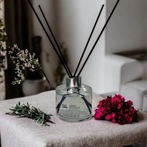 May include: A clear glass diffuser bottle with black reeds and a silver cap. The bottle is labeled "Subtle UAir GREEN HOLIDAYS".