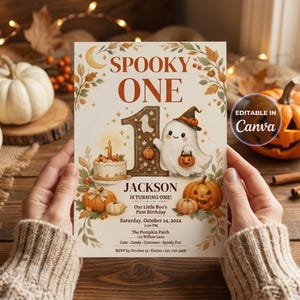 Może przedstawiać: Prostokątne zaproszenie z napisem SPOOKY ONE, dużą cyfrą jeden, duchem w kapeluszu czarownicy, tortem urodzinowym i dyniami. Karta zawiera imię JACKSON, datę, godzinę i miejsce wydarzenia oraz plakietkę EDITABLE IN Canva.