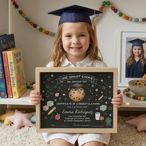 Könnte beinhalten: Ein rechteckiger Holzrahmen mit einem schwarzen Zertifikat mit der Aufschrift One Smart Cookie has graduated. Das Zertifikat zeigt einen Keks mit Doktorhut in der Mitte, umgeben von Illustrationen von Bleistiften, einem Apfel und einem Glas Milch.