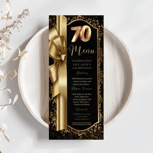 May include: A black and gold 70th birthday menu card featuring a large gold ribbon graphic on the left side. The text reads 70 Menu, Celebrating Lily Anne's 70th Birthday, Starters, Main Course, and Dessert with listed food items and a thank you.