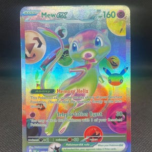 May include: A holographic Mew ex trading card featuring a colorful, iridescent Mew character in the center. The card displays 160 HP, the Memory Helix ability, and the Teleportation Burst attack. It includes various energy symbols and text.
