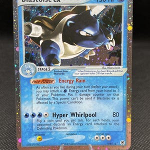 May include: A holographic Blastoise ex trading card with 150 HP. The card features a blue and white Blastoise illustration, the Energy Rain Poke-Power, and the Hyper Whirlpool attack. Text includes Blastoise ex, 150 HP, and 104/112.