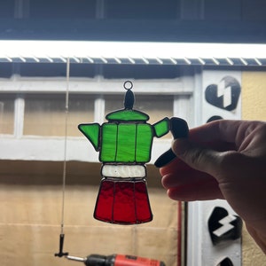 May include: A stained glass hanging ornament shaped like a green, white, and red Italian coffee pot.
