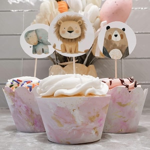 May include: Three pink and gold cupcake wrappers with white frosting. Each cupcake has a different animal topper: a lion, an elephant, and a bear.