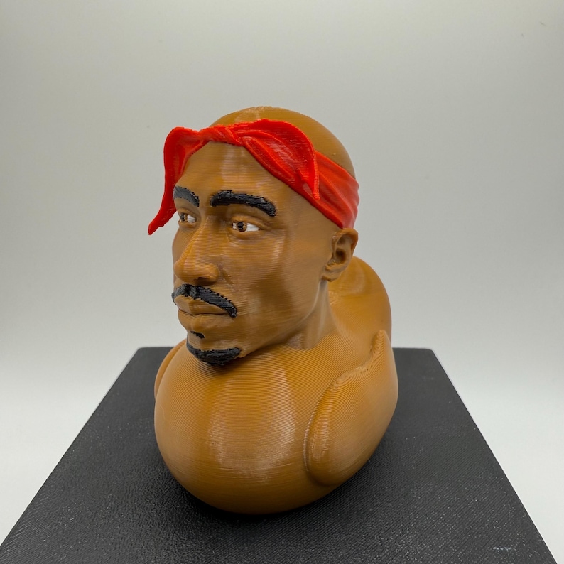 May include: A brown 3D-printed bust of a man with a red bandana. The bust has a mustache and a detailed facial structure. The bust is sitting on a black surface.