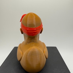 May include: A 3D-printed bust of a person with a red headband. The bust is a light brown color and has a smooth, rounded shape. The headband is a bright red and wraps around the head.