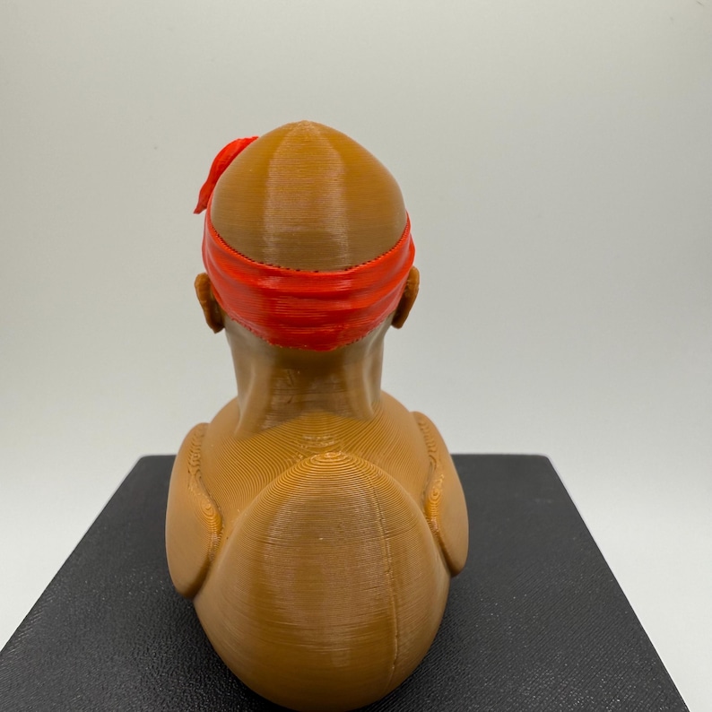May include: A 3D-printed bust of a person with a red headband. The bust is a light brown color and has a smooth, rounded shape. The headband is a bright red and wraps around the head.