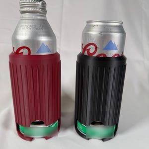 May include: Two beverage insulators, one burgundy and one black, each holding a silver can. The insulators have a ribbed design and a cutout at the bottom. The cans have a blue mountain logo.