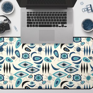 Op de afbeelding: Een bureauonderlegger met een retro modern design uit het midden van de eeuw, met een herhalend patroon van blauwe, turquoise en zwarte abstracte vormen op een cr&egrave;me achtergrond.