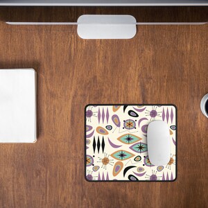 Op de afbeelding: Een witte computermuis ligt op een muismat met een retro mid-century modern design met abstracte vormen in tinten paars, oranje en bruin op een cr&egrave;mekleurige achtergrond.