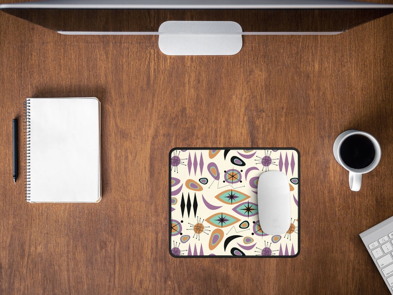 Op de afbeelding: Een witte computermuis ligt op een muismat met een retro mid-century modern design met abstracte vormen in tinten paars, oranje en bruin op een cr&egrave;mekleurige achtergrond.