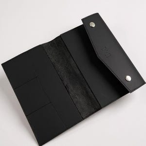May include: Open black leather wallet with multiple card slots and a snap closure. The wallet is rectangular and has a smooth texture. The brand name "BRUME" is embossed on the flap.