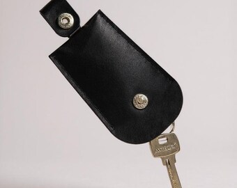 May include: Black leather key holder with a silver snap closure and a single key attached. The key is silver and has the word "Artec" printed on it. The key holder is rectangular with rounded edges.