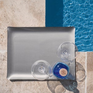 Plateau acrylique couleur argent placé en bord de piscine avec 2 verres et une bouteille