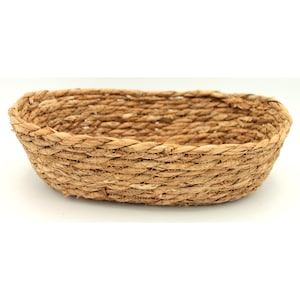 Può includere: Un cesto ovale intrecciato in fibre naturali. Il cesto è di colore marrone chiaro e ha una superficie liscia leggermente ruvida.