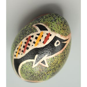 Pode incluir: Um ovo de Páscoa verde salpicado com um desenho pintado em preto e branco de um peixe com acentos vermelhos e amarelos.