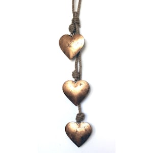 May include: A string of three gold metal hearts hanging from a natural jute rope. The hearts are connected by knots in the rope.