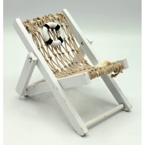 Peut inclure: Chaise longue de plage en bois blanc avec un siège en filet de corde et un sauveteur de vie blanc et noir. La chaise est pliée et a une petite coquille blanche sur le siège.