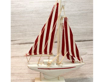 May include: A small white wooden sailboat with red and white striped sails. The sailboat is on a white wooden base.