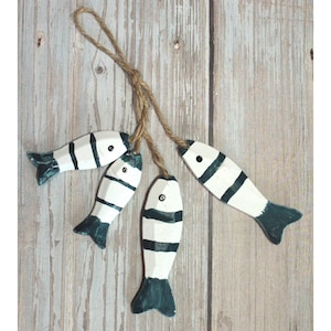 Könnte beinhalten: Ein Set aus vier Holzfischen, die weiß mit schwarzen Streifen und grünen Schwänzen bemalt sind. Die Fische sind mit einer Schnur zusammengefügt und zum Aufhängen bereit.