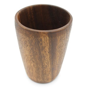 Könnte beinhalten: Eine dunkelbraune Holztasse mit glattem, abgerundetem Innenraum. Die Tasse ist aus Naturholz gefertigt und hat ein rustikales, handgefertigtes Aussehen.