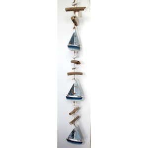 Pode incluir: Um pendurado de parede com tema náutico com uma corda de barcos à vela azuis e brancos, madeira flutuante e pedras brancas. Os barcos à vela são pintados com um visual desgastado e têm um charme rústico.