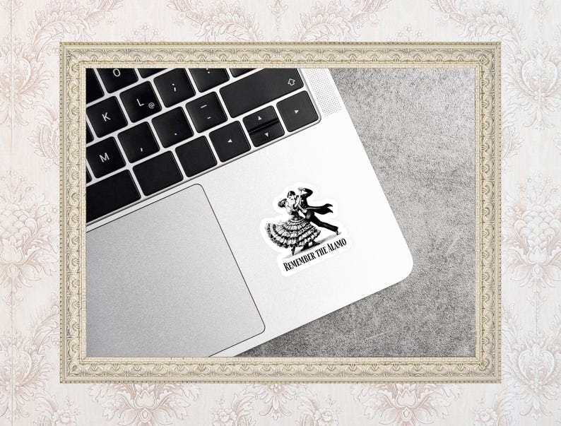 May include: A black and white sticker featuring a couple dancing, with the text "REMEMBER THE ALAMO." The sticker is placed on a silver laptop. The laptop keyboard is visible.