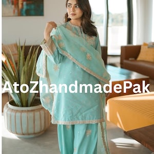 May include: A light blue salwar kameez set with intricate embroidery and embellishments. The set includes a tunic, pants, and a matching scarf. The outfit features gold trim and delicate detailing, perfect for special occasions.