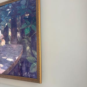 May include: A framed painting with a gold-colored ornate frame. The artwork depicts a landscape scene with trees, foliage, and a table. The painting is signed "M. Eyner" in the lower right corner. The color palette includes shades of blue, green, and purple.