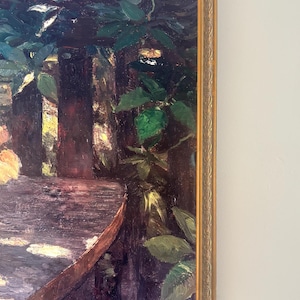 Pode incluir: Pintura a óleo emoldurada em ouro retratando uma cena de jardim com uma mesa e folhagem exuberante. A obra apresenta uma paleta de cores escuras com pinceladas visíveis, assinada "M. Eyner" no canto inferior direito. A moldura tem um design ornamentado e texturizado.