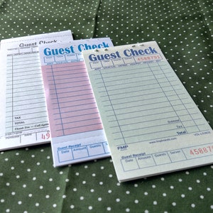 May include: Three blank guest checks with the text "Guest Check" printed on them. The checks are on a green and white polka dot tablecloth. The top check has the number 49 printed on it. The bottom check has the number 4588791 printed on it.