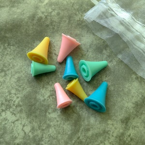 May include: A set of seven colorful plastic needle threaders in a variety of colors including pink, blue, green, and yellow. The threaders are in a small white mesh bag.
