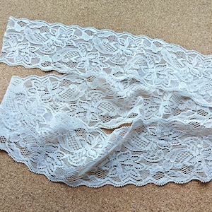 May include: White lace trim with a delicate floral pattern. The lace is soft and flexible, making it ideal for a variety of crafting projects.
