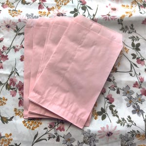 May include: A stack of five pink paper envelopes, folded and ready to be used for mailing letters or small items.