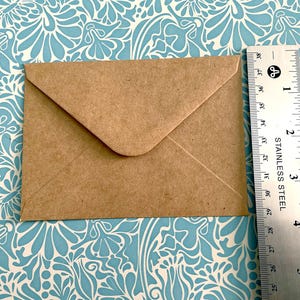 May include: A brown paper envelope with a white flap. The envelope is lying flat on a blue and white patterned surface.