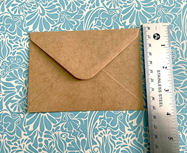 May include: A brown paper envelope with a white flap. The envelope is lying flat on a blue and white patterned surface.