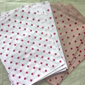 May include: Stacks of white and tan polka dot tissue paper. The white paper has red dots, and the tan paper has red dots. The paper is arranged in stacks, with the polka dots clearly visible. The paper is likely used for wrapping gifts or crafts.