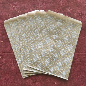 May include: A stack of six brown paper gift bags with a white damask pattern. The bags are folded and ready to be used.