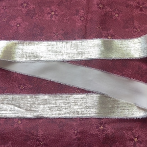 May include: A silver ribbon with a white backing. The ribbon has a slightly frayed edge.
