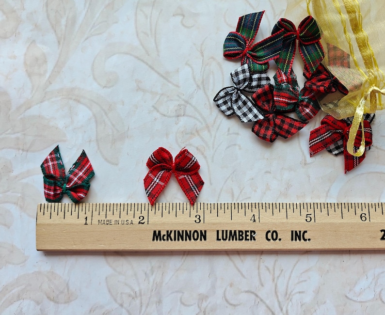 May include: Various miniature plaid bows in red, green, black, and white. A wooden ruler with inch markings and the text "MADE IN U.S.A." and "McKINNON LUMBER CO. INC." is in the foreground. The bows are scattered on a patterned surface.