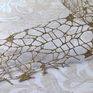 May include: Gold glitter spiderweb ribbon with a delicate, intricate design. The ribbon is made of a sheer material and has a sparkly finish.