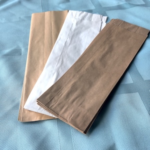 May include: Three paper bags, one white and two brown, are stacked on top of each other on a blue patterned surface.