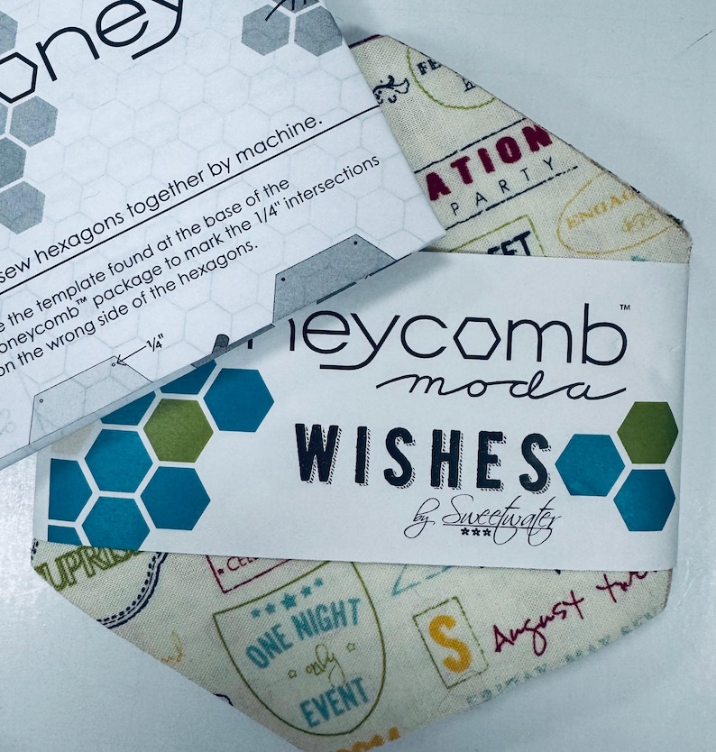 May include: Honeycomb Moda fabric package with the word "Wishes" and a geometric design in teal, green, and white. The package includes instructions and a fabric piece with travel-themed stamps.