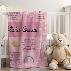 May include: A pink baby blanket with the name "Olivia Grace" in black script. The blanket features a sun, rainbow, stars, and floral designs, along with Bible verses. A teddy bear sits next to the blanket.