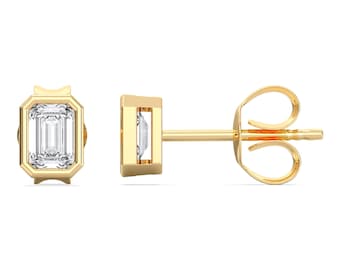 May include: A pair of gold stud earrings, each featuring a rectangular, clear gemstone. The gemstones are set in a gold bezel setting. The earrings are displayed on a white background.